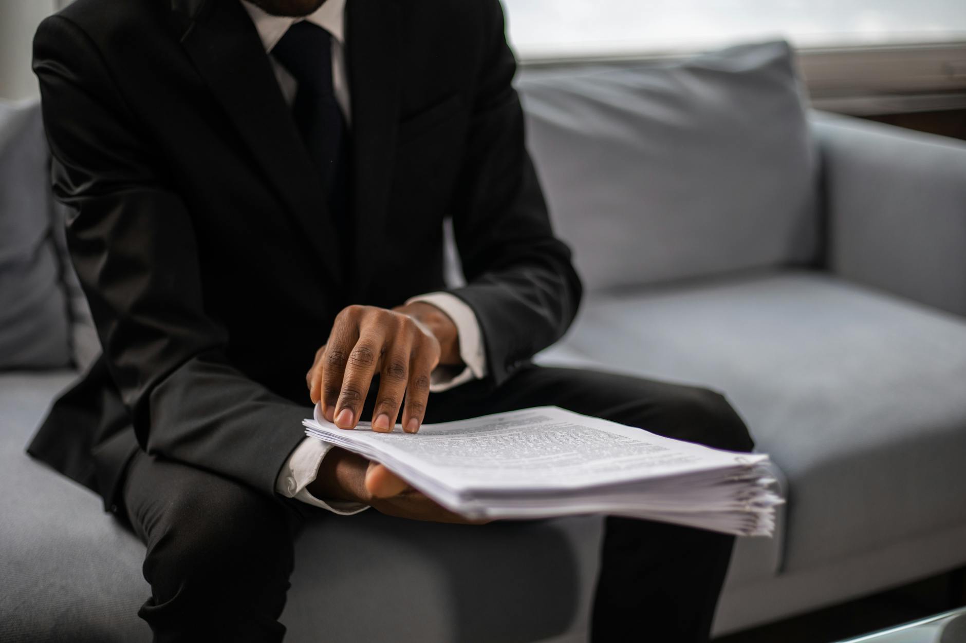 Close-up of a businessman in a suit reviewing documents while seated on a sofa indoors.