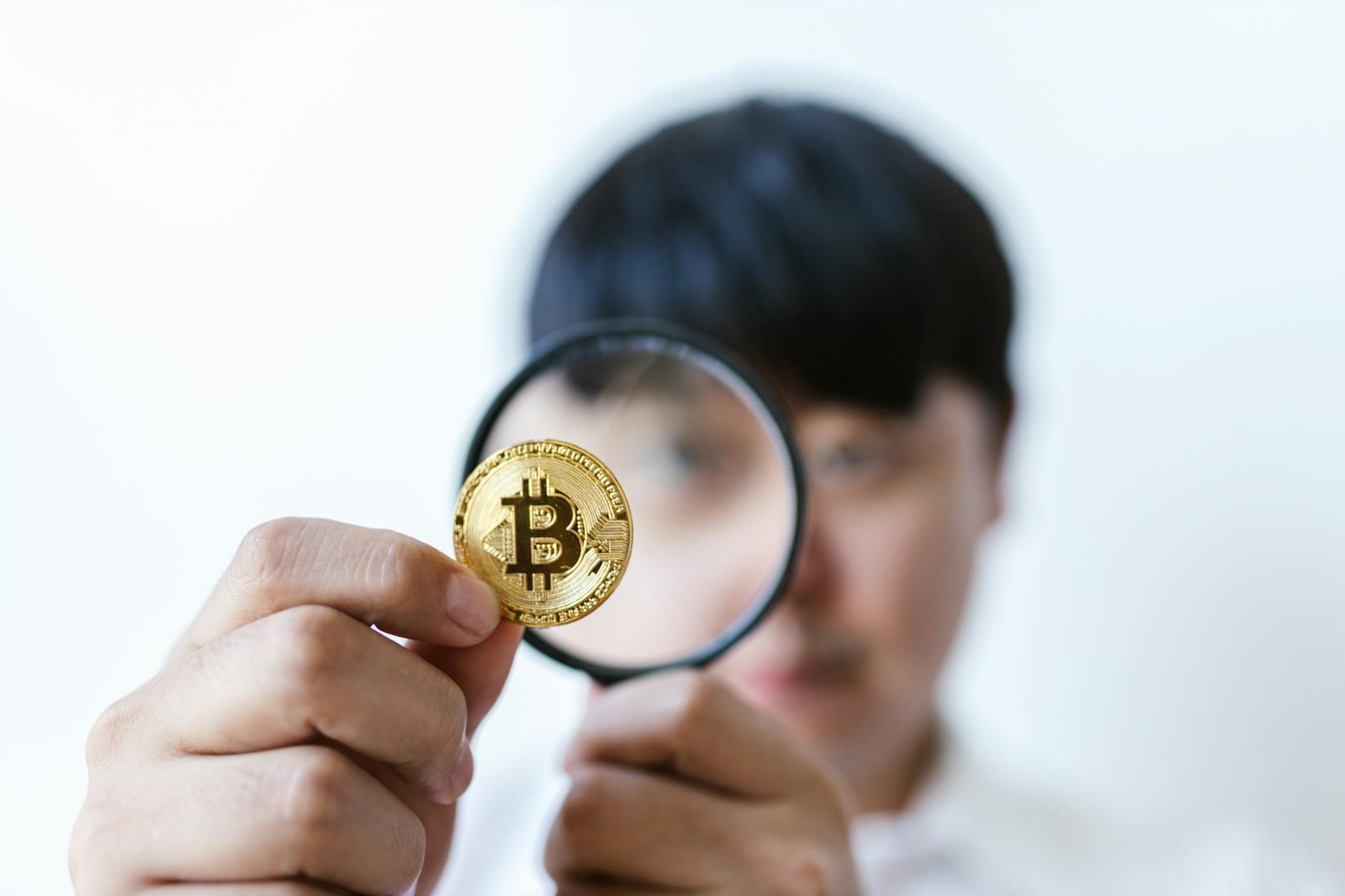 Close-up of a person examining a Bitcoin with a magnifying glass, highlighting cryptocurrency focus.