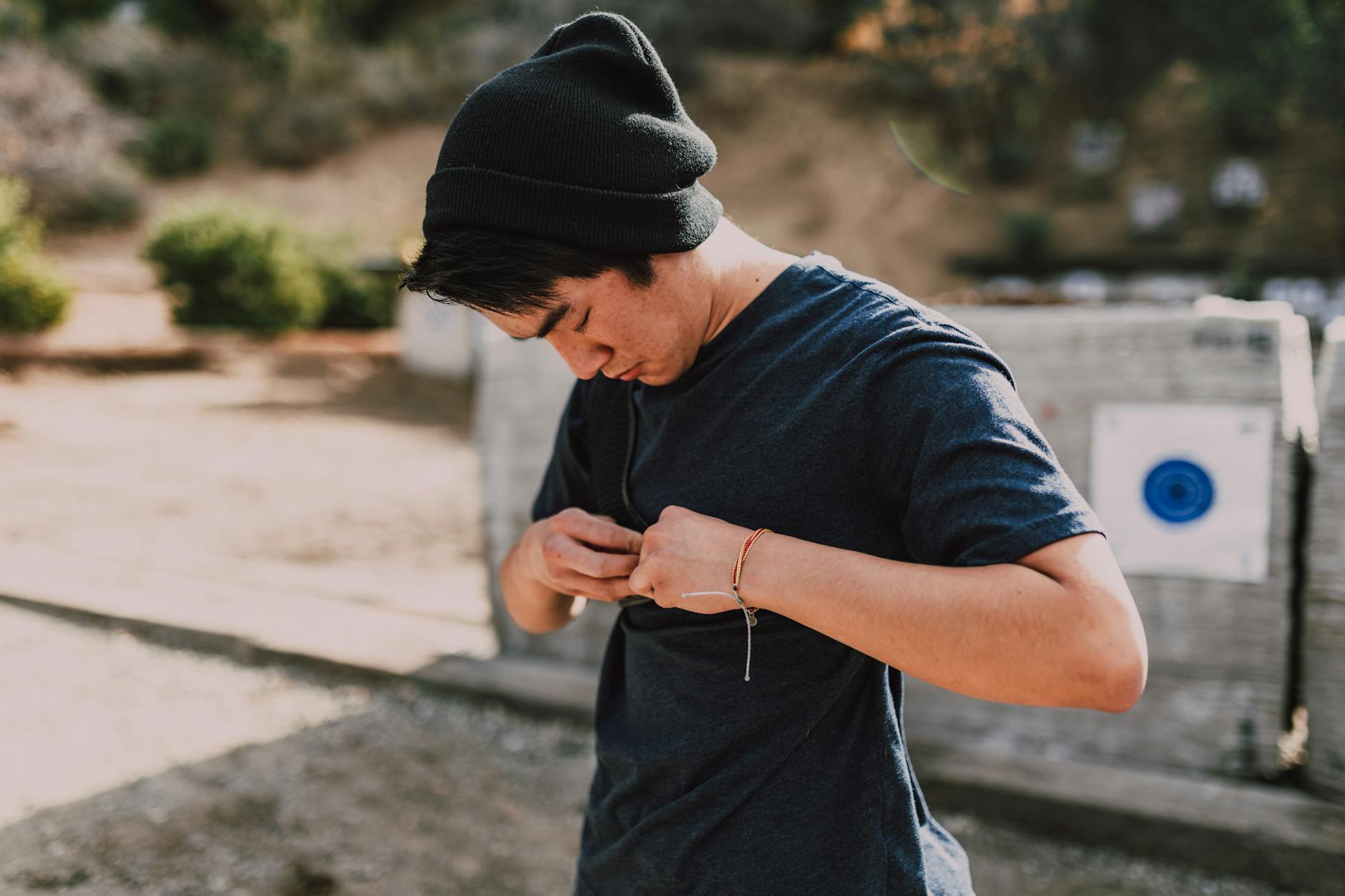 Youth adjusting bowstring at an outdoor archery range, enjoying a sunny day.